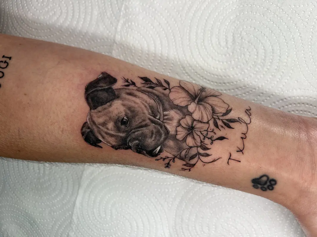 Retrato de perro con flores y lettering en el antebrazo, estilo blackwork.