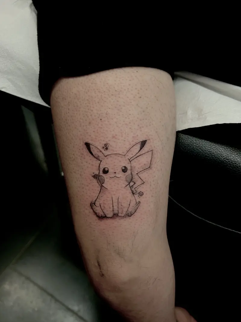 Personaje estilo Pokémon en tatuaje pequeño, tinta negra.
