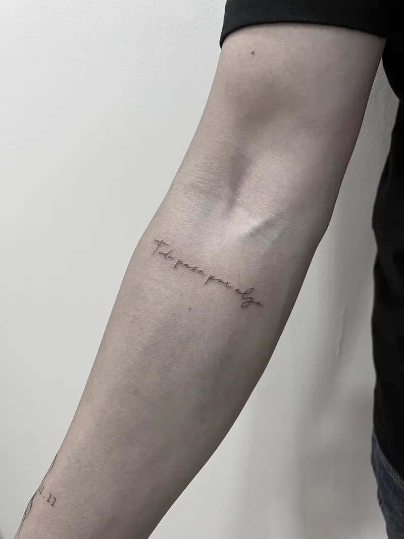 Frase corta en caligrafía fina sobre el antebrazo, estilo escritura manuscrita muy sutil.