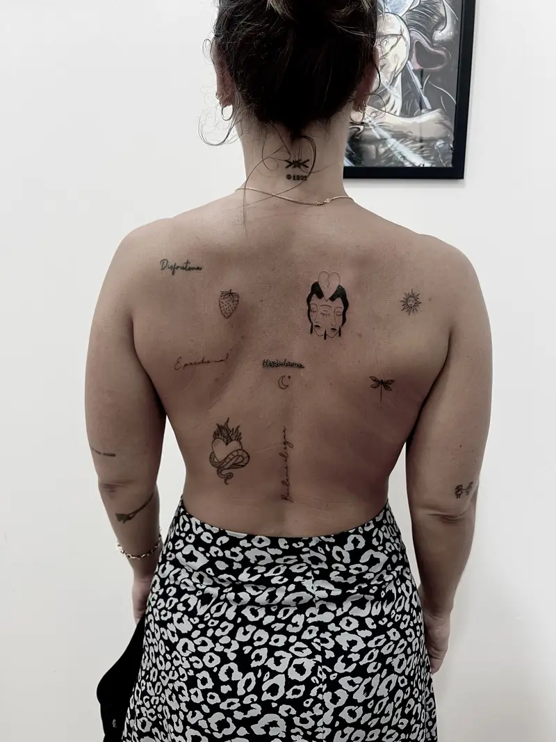 Constelación de mini tatuajes en la espalda: símbolos, insecto, fruta, carita ilustrada y palabras en diferentes estilos.
