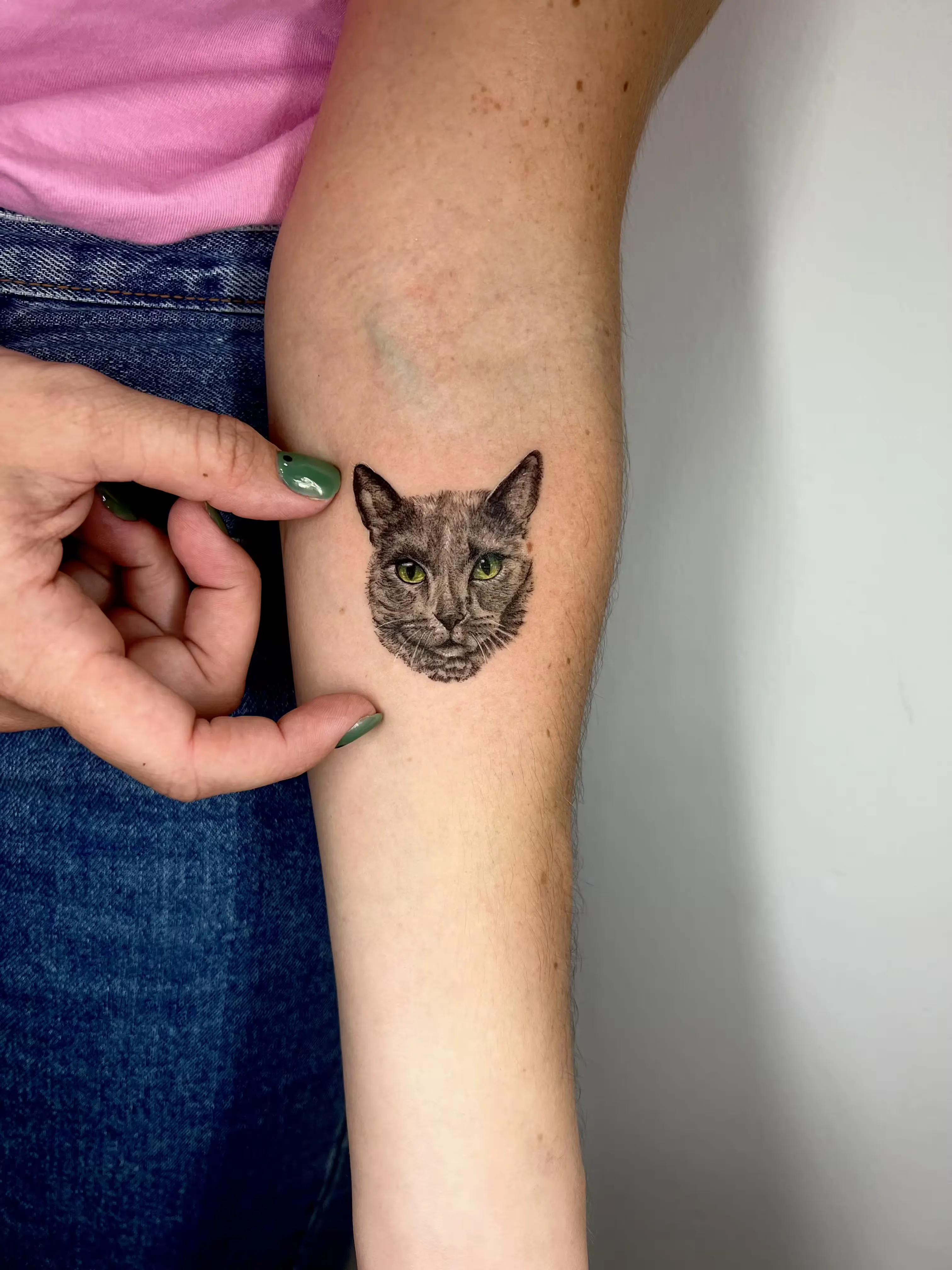 Micro retrato realista de gato en black and grey con ojos verdes, mostrado a escala con la mano.